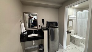 A compact bathroom with a sink, mirror, and a microwave on a small refrigerator.