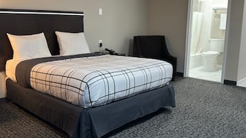 A hotel room with a large bed, a chair, and a bathroom visible through an open door.