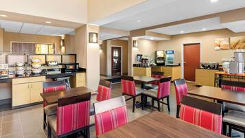 A modern hotel dining area with wooden tables and red upholstered chairs, equipped with coffee machines and a buffet.