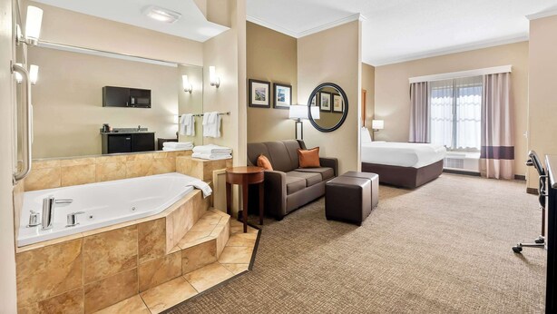 A hotel room with a large bathtub, a sofa, a small table, a bed, and a large mirror. - Comfort Suites (Panama City)
