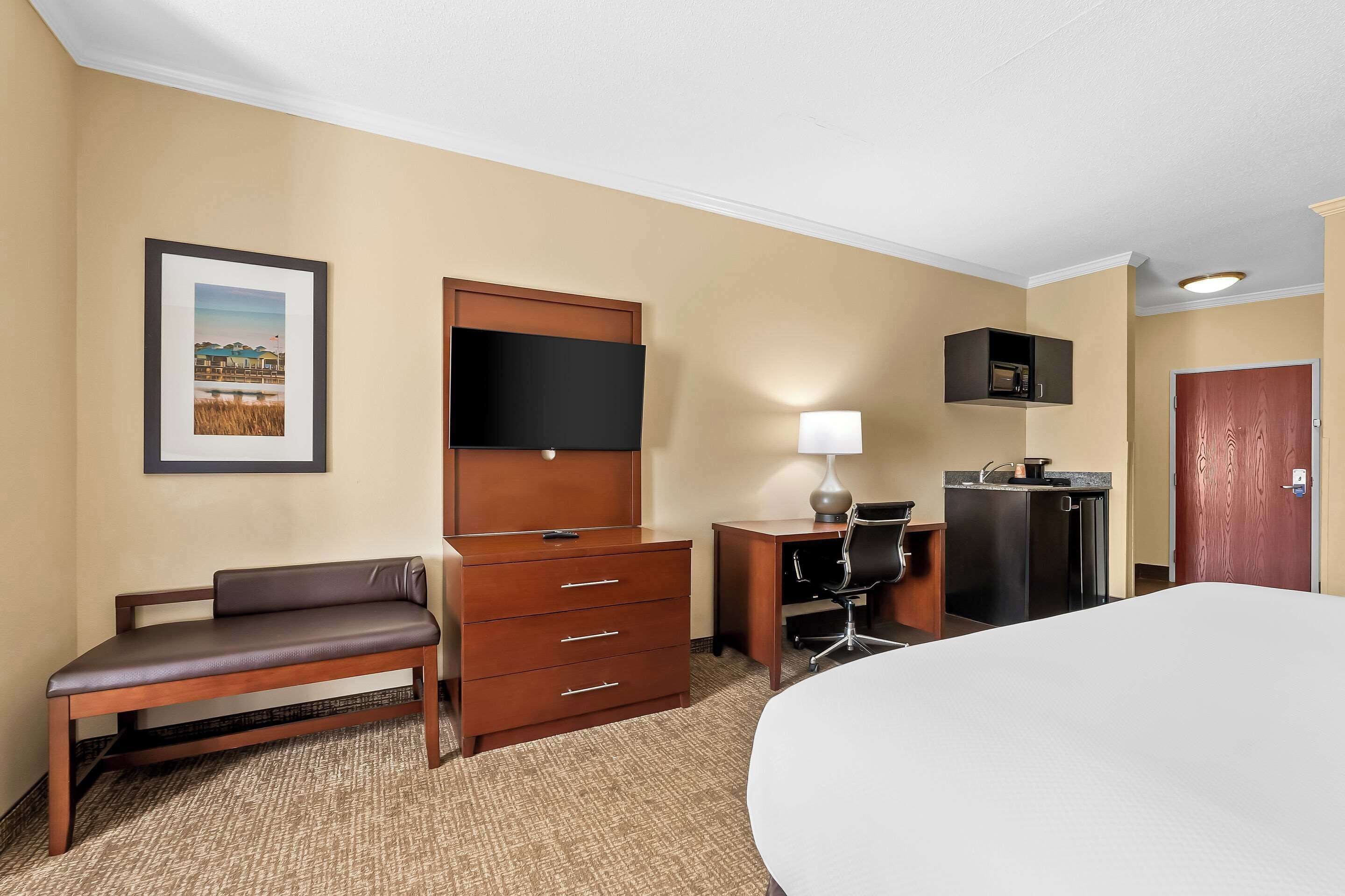 Una habitación de hotel con una cama, un escritorio con silla, un aparador, un televisor, una lámpara y un microondas.