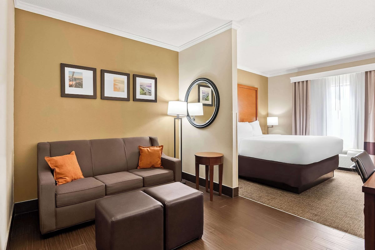 A hotel room with a brown leather sofa, a bed, a small round table, and a wall-mounted mirror.