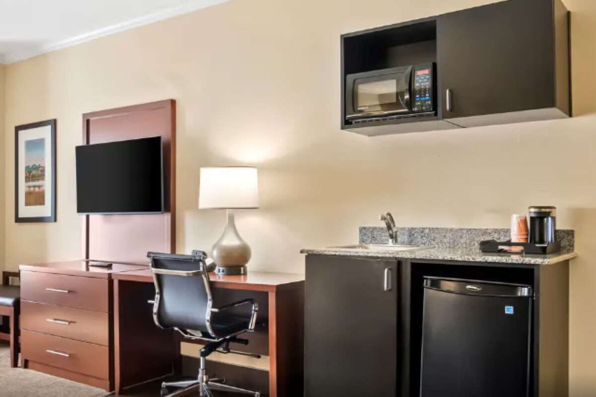 A hotel room with a desk, chair, television, lamp, microwave, and refrigerator.