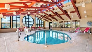 An indoor swimming pool with red beams, large windows, and sunlit areas with lounge chairs. - Comfort Suites (Panama City)