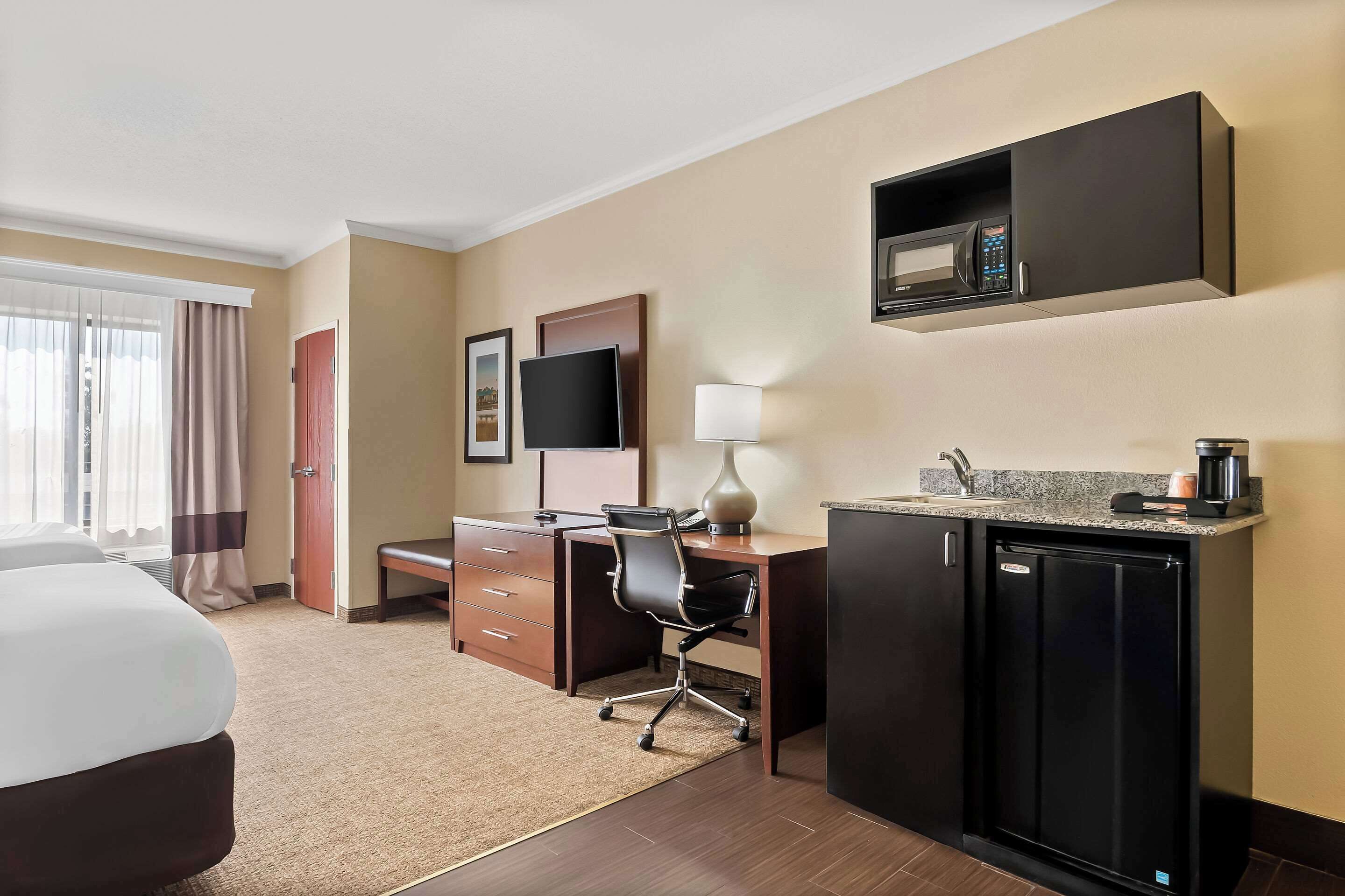 Una habitación de hotel con cama, escritorio, silla, kitchenette y televisor.