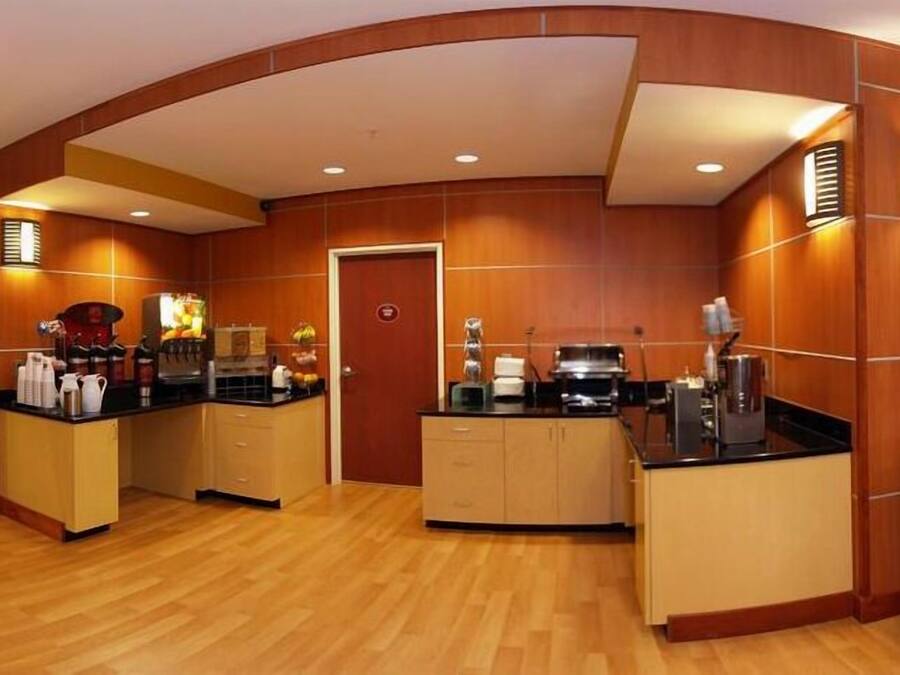 A hotel lobby with a curved wooden reception desk, a coffee station, and a trash can.