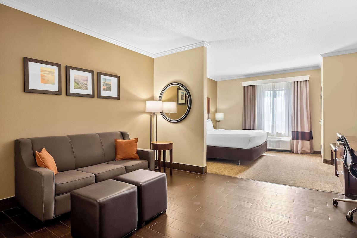 A hotel room with a sofa, ottoman, a round mirror, a bed, and a desk.