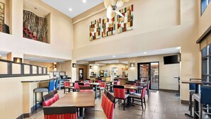 A spacious hotel dining area with multiple tables and chairs, a kitchen in the background, and artwork on the walls. - Comfort Suites (Panama City)