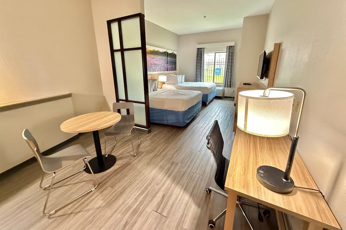 Una habitación de hotel con una cama, un escritorio con lámpara, una silla y una mesita.