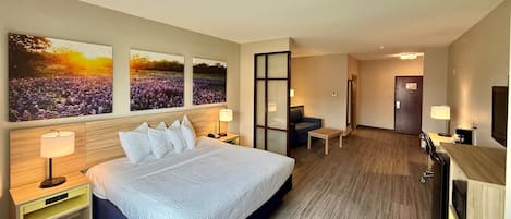 A hotel room with a large bed, two bedside tables with lamps, a desk, a chair, and a TV. There are three large wall art pieces above the bed.