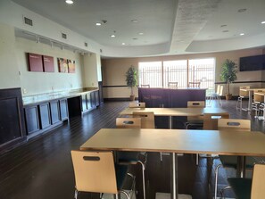 A spacious dining area with high tables and chairs, a kitchen counter, and a large window allowing natural light.