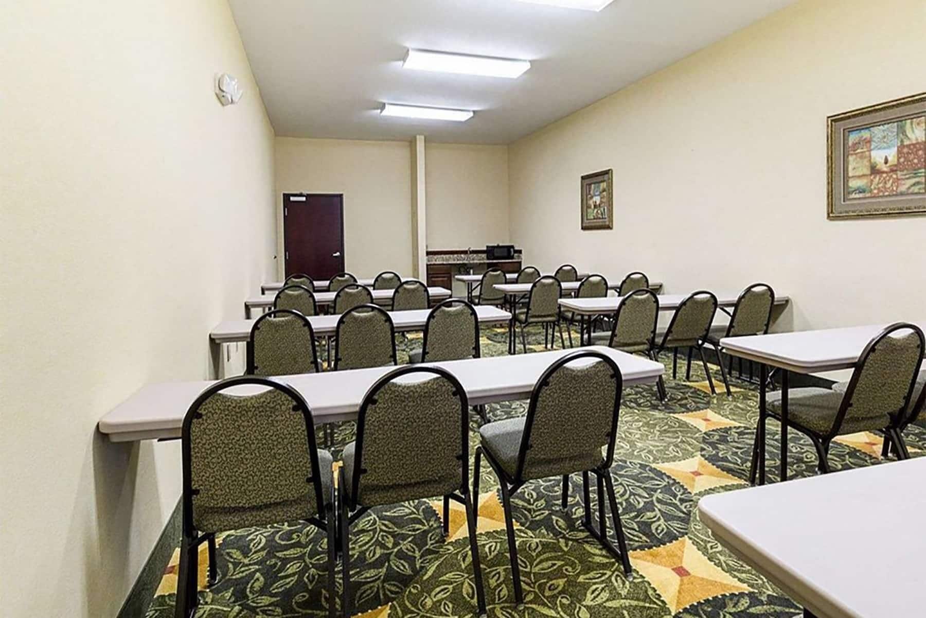 Una sala de conferencias con varias mesas y sillas, una puerta y un microondas sobre una encimera.