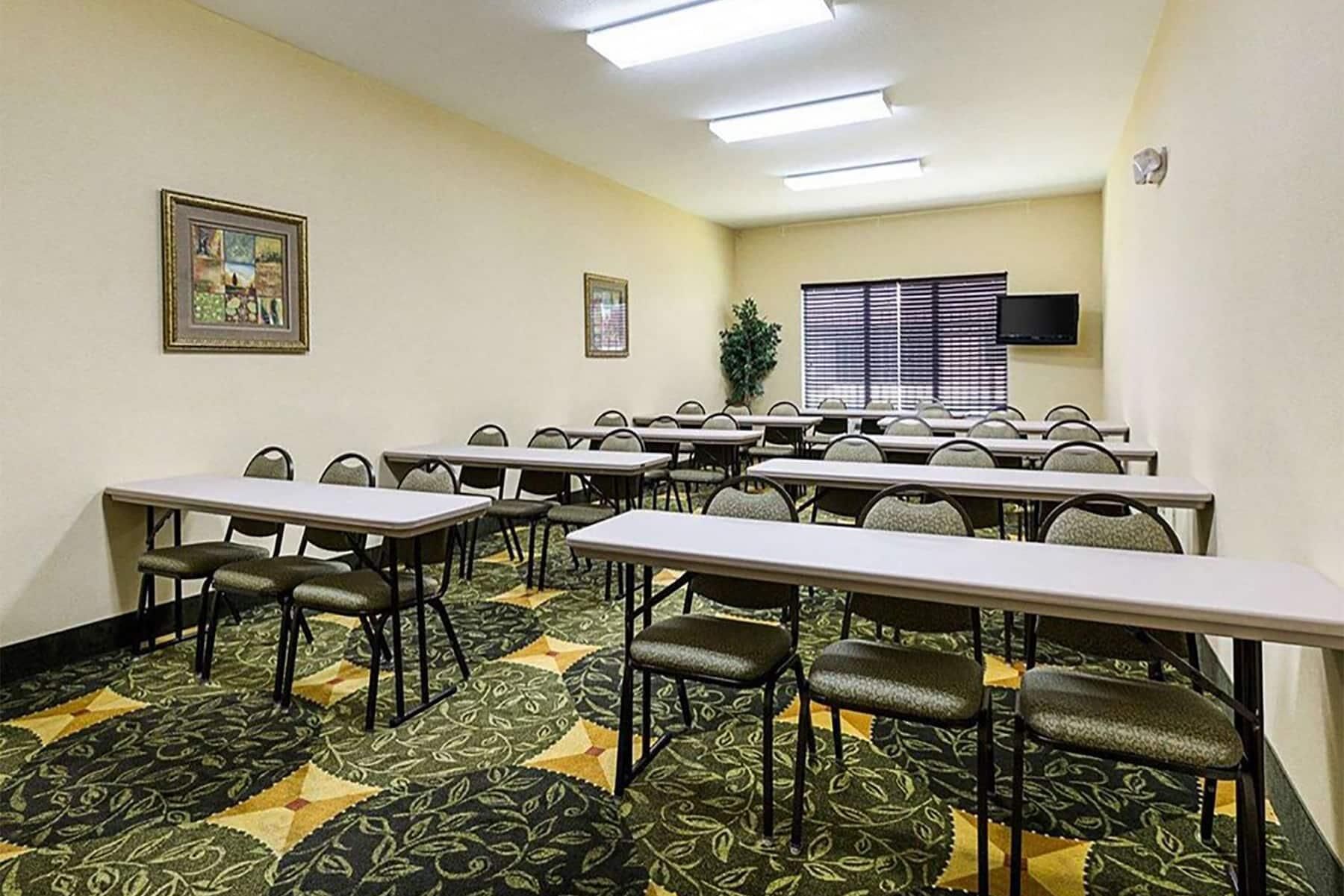 Una sala de conferències amb diverses taules i cadires, una finestra gran amb persianes i un televisor penjat.