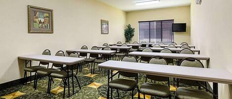 A conference room with multiple tables and chairs, a large window with blinds, and a mounted television.