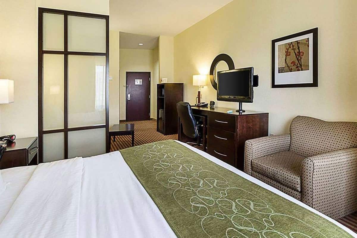 Habitación de hotel con cama, escritorio, computadora, silla, televisor y puerta.