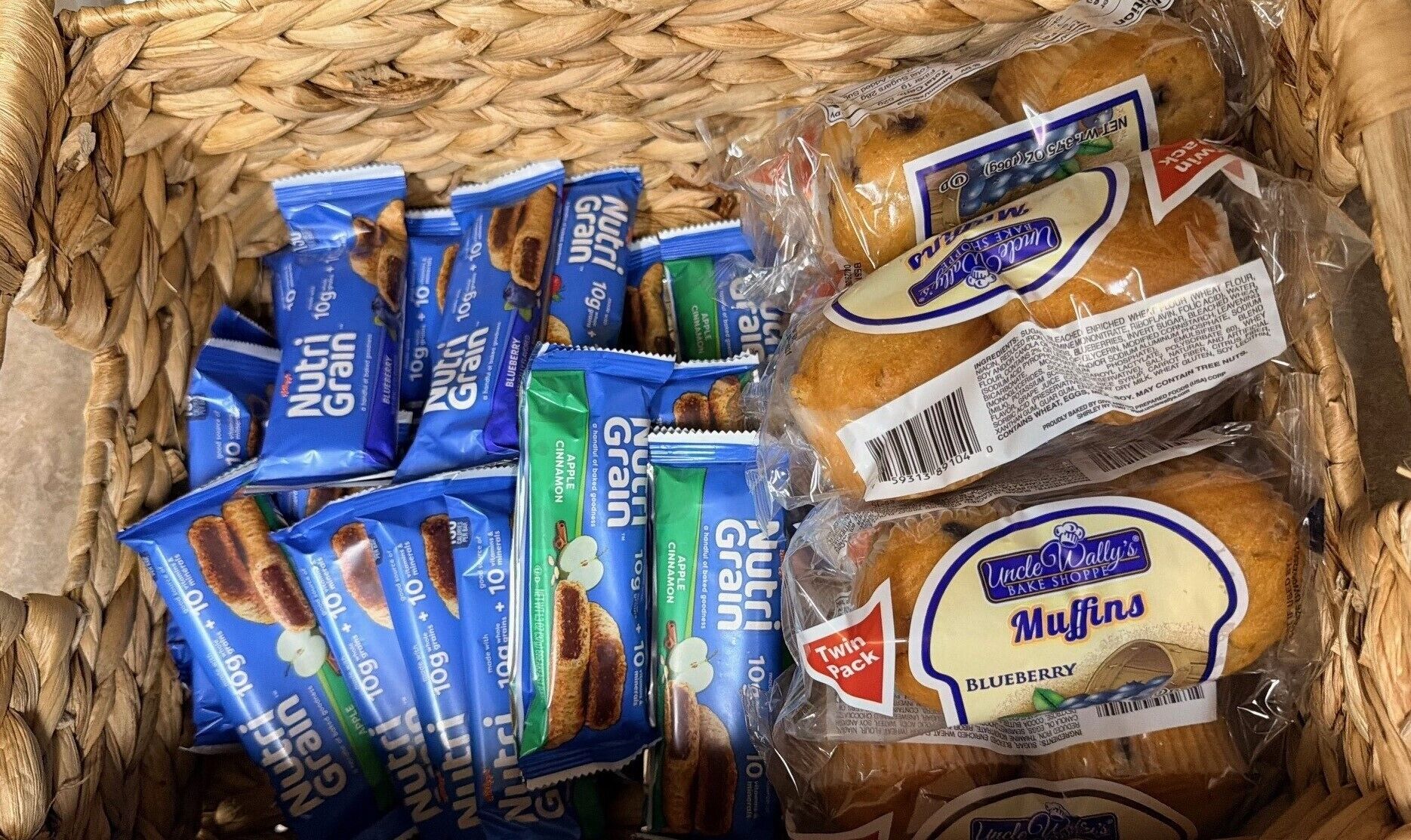 En kurv med forskelligt mad, herunder pakker med snacks, muffins og brød.