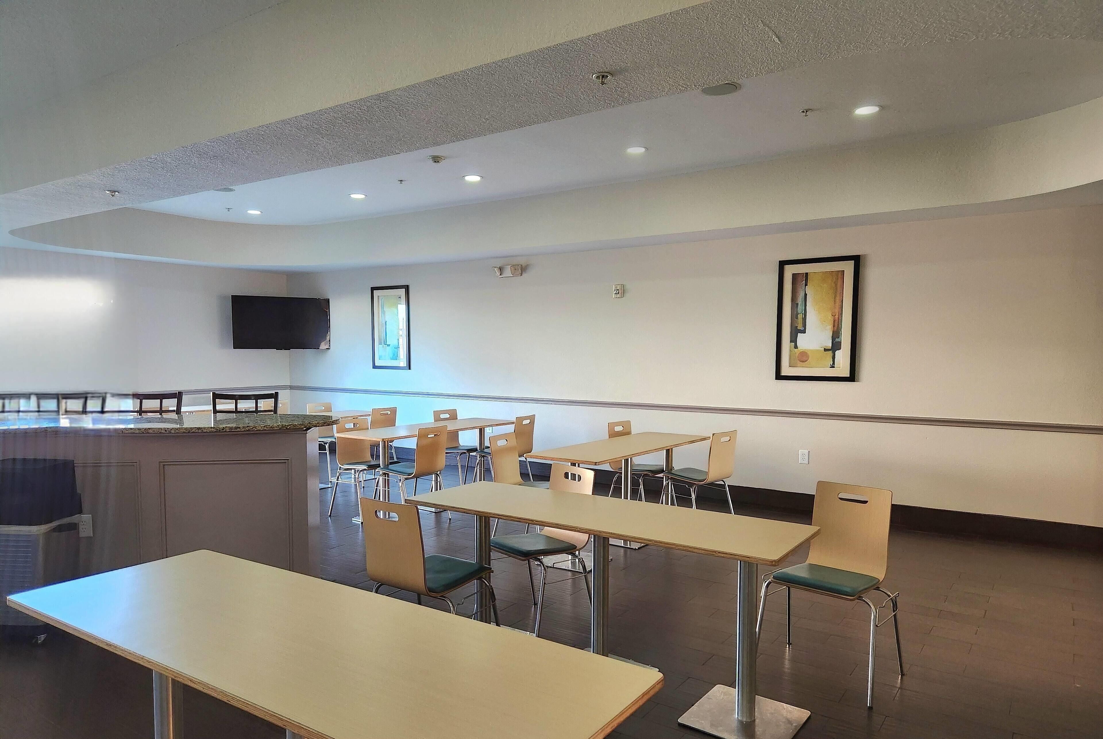 A modern dining area with tables and chairs, a flat-screen TV mounted on the wall, and a painting.