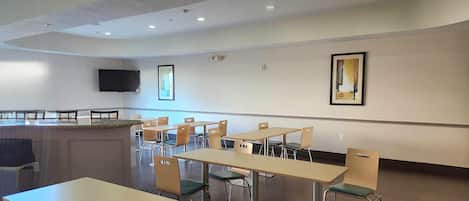 A modern dining area with tables and chairs, a flat-screen TV mounted on the wall, and a painting.