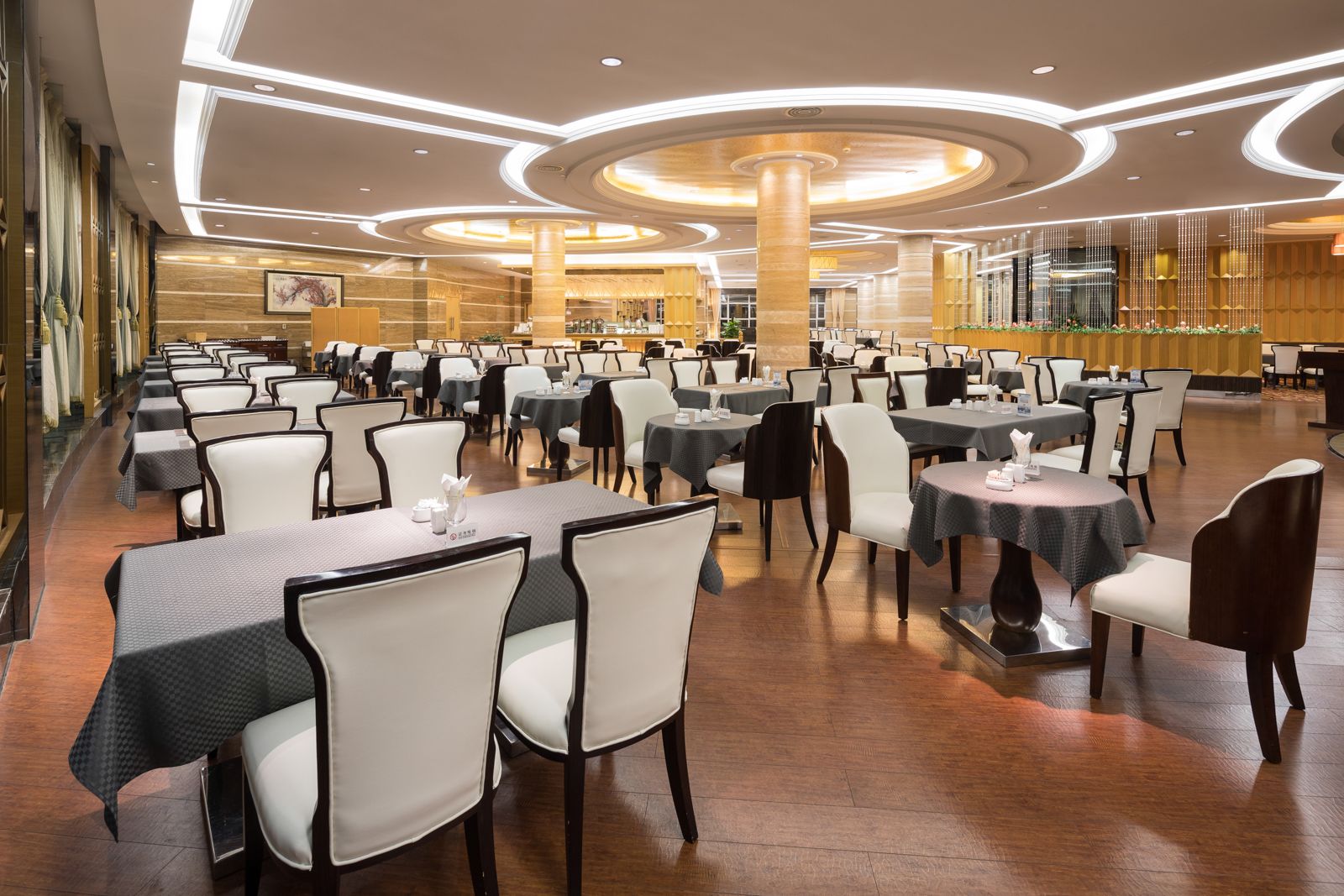 Ein geräumiger Essbereich mit mehreren Tischen und Stühlen, ausgestattet mit einem modernen Deckenstil und runden Leuchten.