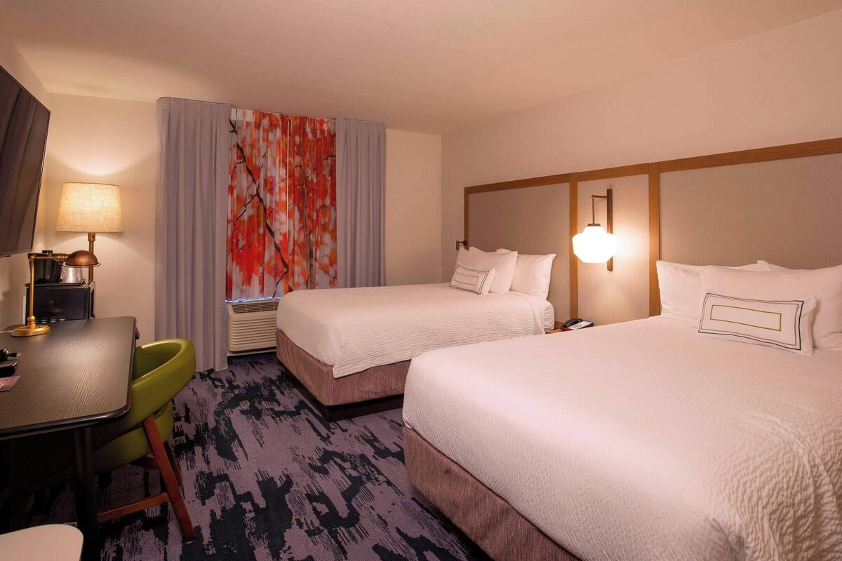 A hotel room with two beds, a desk, a chair, and a large window with curtains.