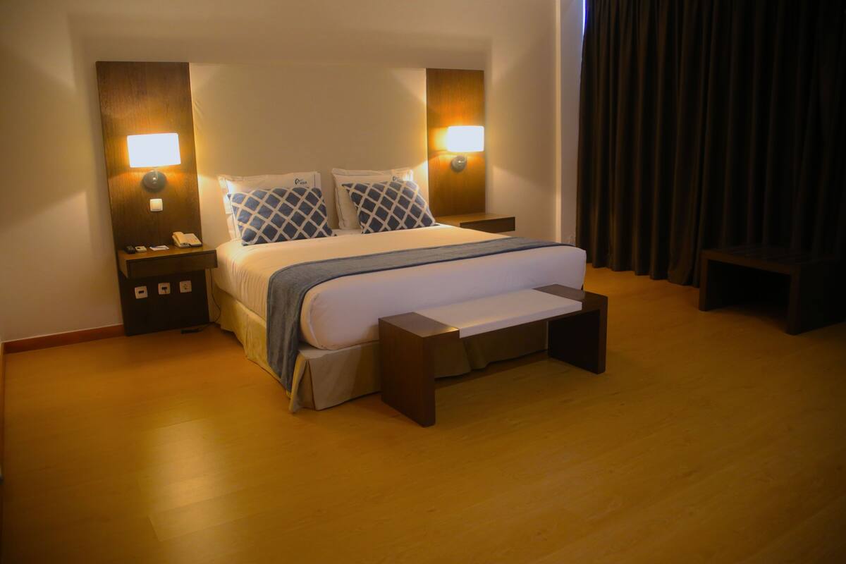 A hotel room with a large bed, bedside lamps, a bedside table, and a wooden floor.