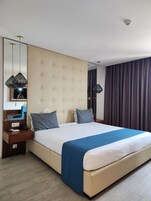 Habitación de hotel con una cama grande, una mesita de noche con lámpara, un televisor de pantalla plana y un espejo.
