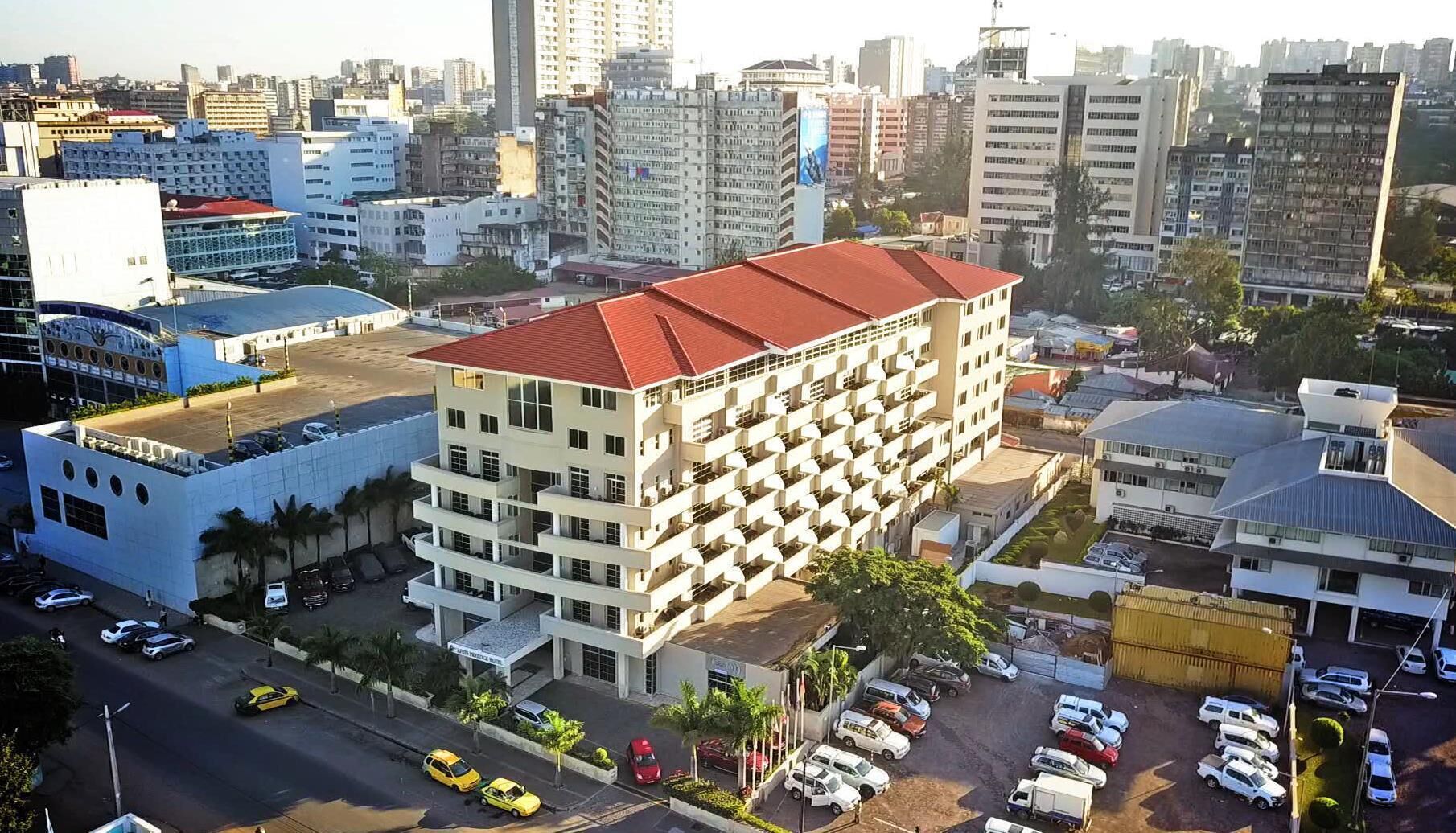 Um hotel de vários andares com telhado vermelho, cercado por outros edifícios e carros estacionados.