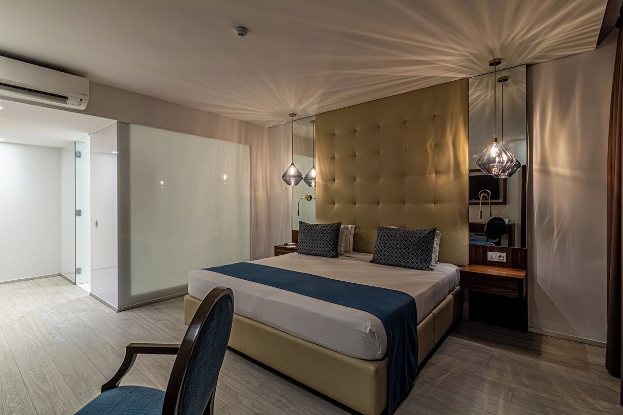 A modern hotel room with a large bed, a seating area, and a vanity with a mirror.