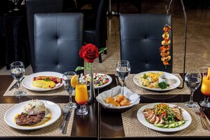 Una mesa de comedor con diversos platos, incluyendo bistec, ensalada y brochetas de mariscos, sobre un tablero de madera oscura con individuales trenzados.