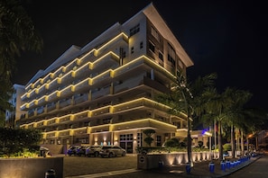 A multi-story hotel with a modern design, featuring balconies with illuminated railings and a parking area with several cars. - Afrin Prestige (Maputo)