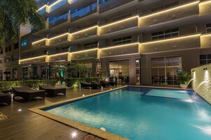 Un hotel con piscina, mobiliario exterior y un edificio de varios pisos con balcones.