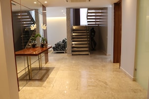 Un interior moderno con suelo de mármol, un banco de madera, una mesa de vidrio con orquídeas y una escalera con barandilla de metal.