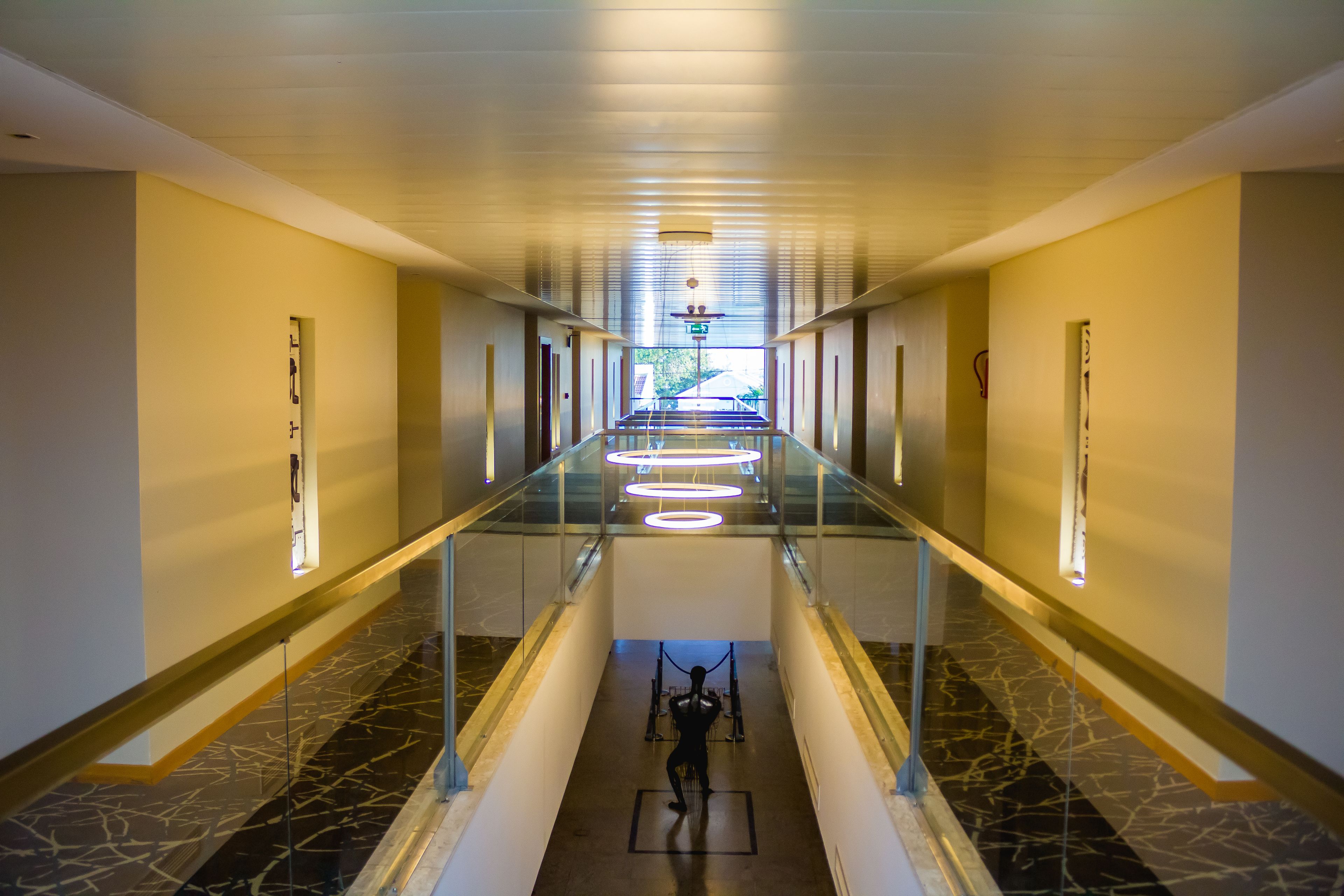 A long, well-lit corridor with a glass railing, leading to a staircase.