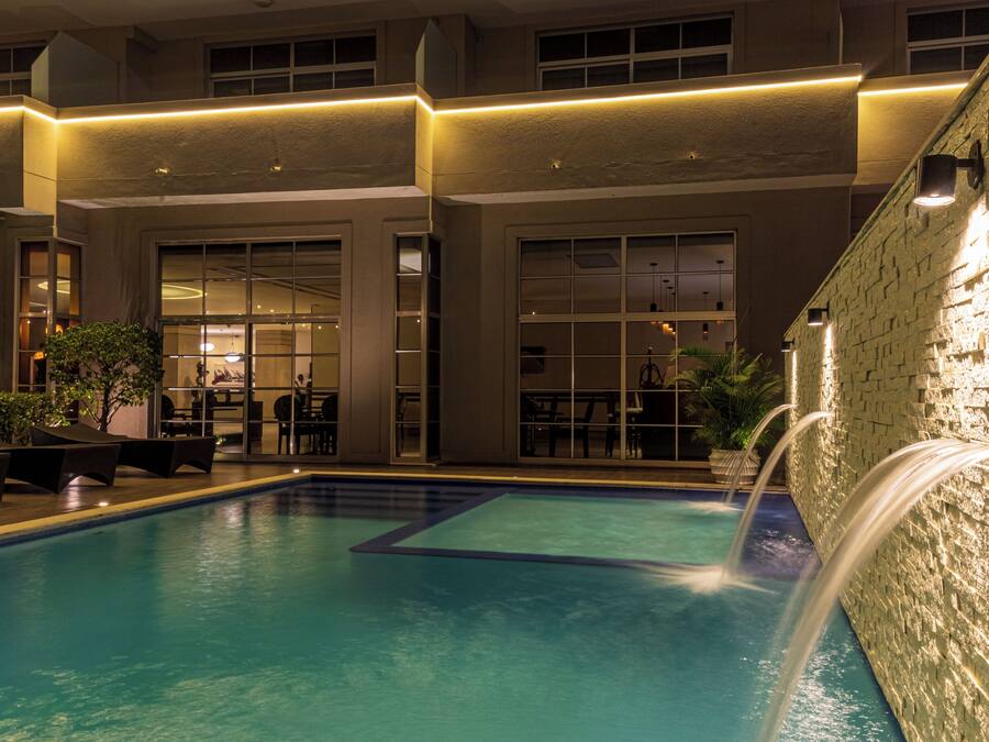 A swimming pool with a waterfall feature, surrounded by a building with large windows and indoor seating areas.