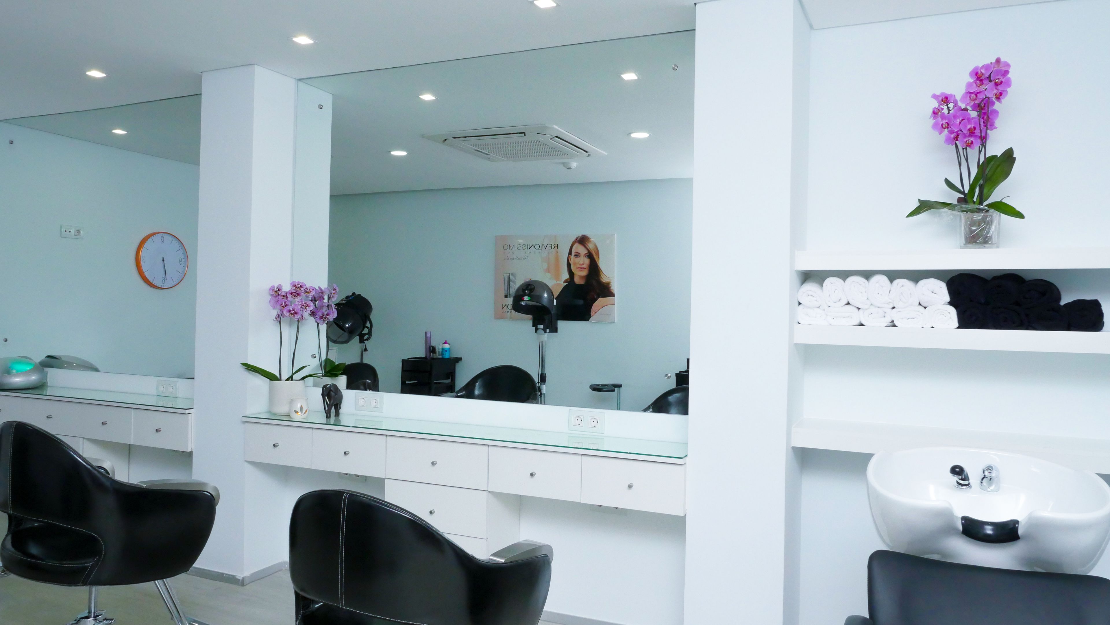 A modern salon with a large mirror, black chairs, a sink, and shelves with towels.