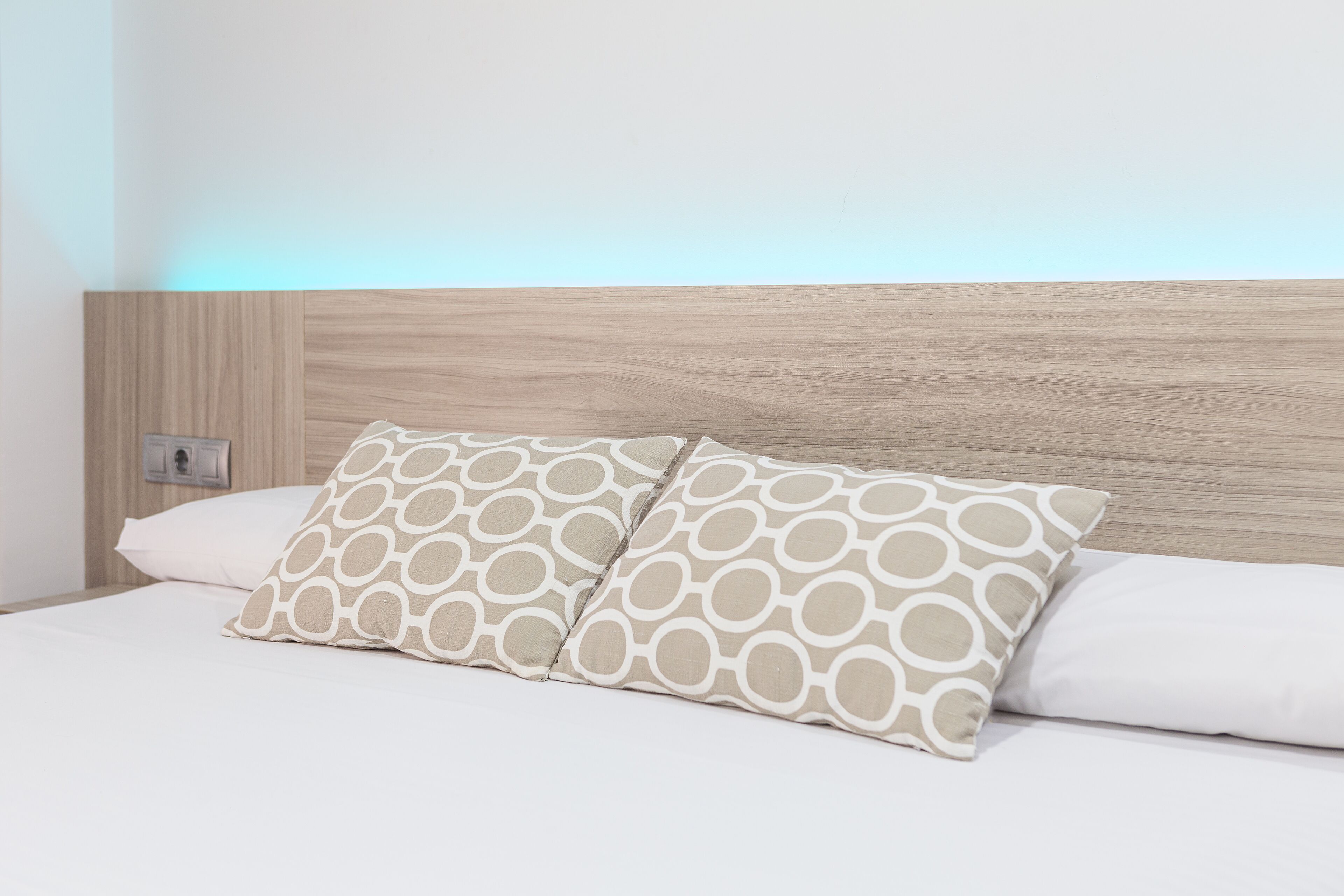 Una cama con dos almohadas, cabecera de madera y un enchufe de pared.