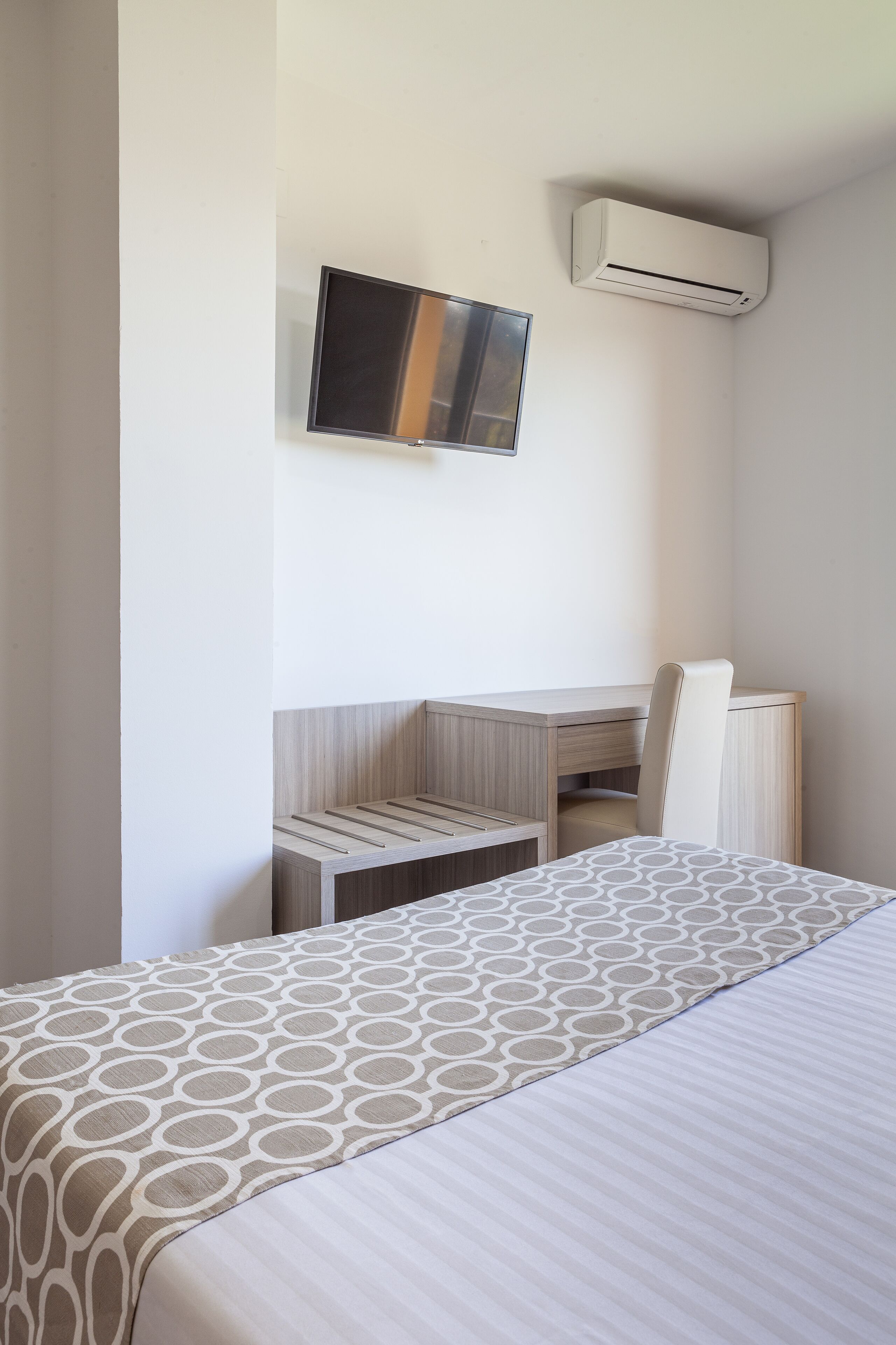 Een hotelkamer met een bed, bureau, stoel, televisie en airconditioning.