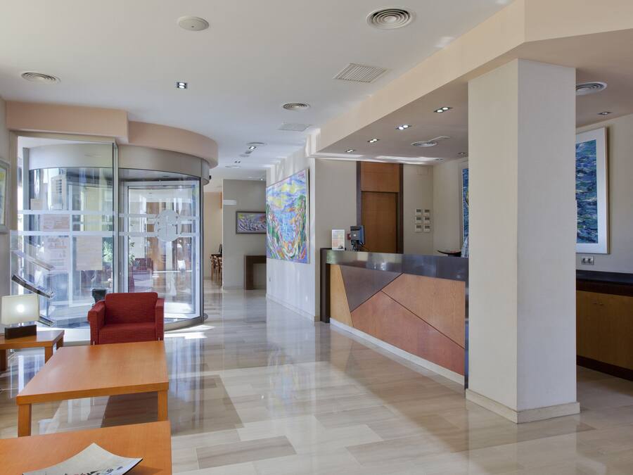 Un hall d’hôtel moderne avec un comptoir d’accueil, un espace salon et des portes vitrées donnant sur un couloir.