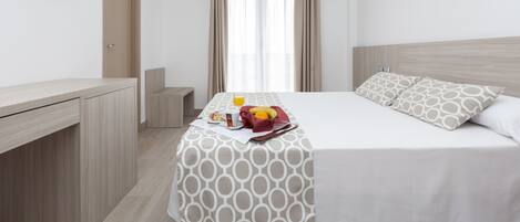 Habitación de hotel con cama, escritorio, televisor y bandeja de desayuno con frutas y una bebida.