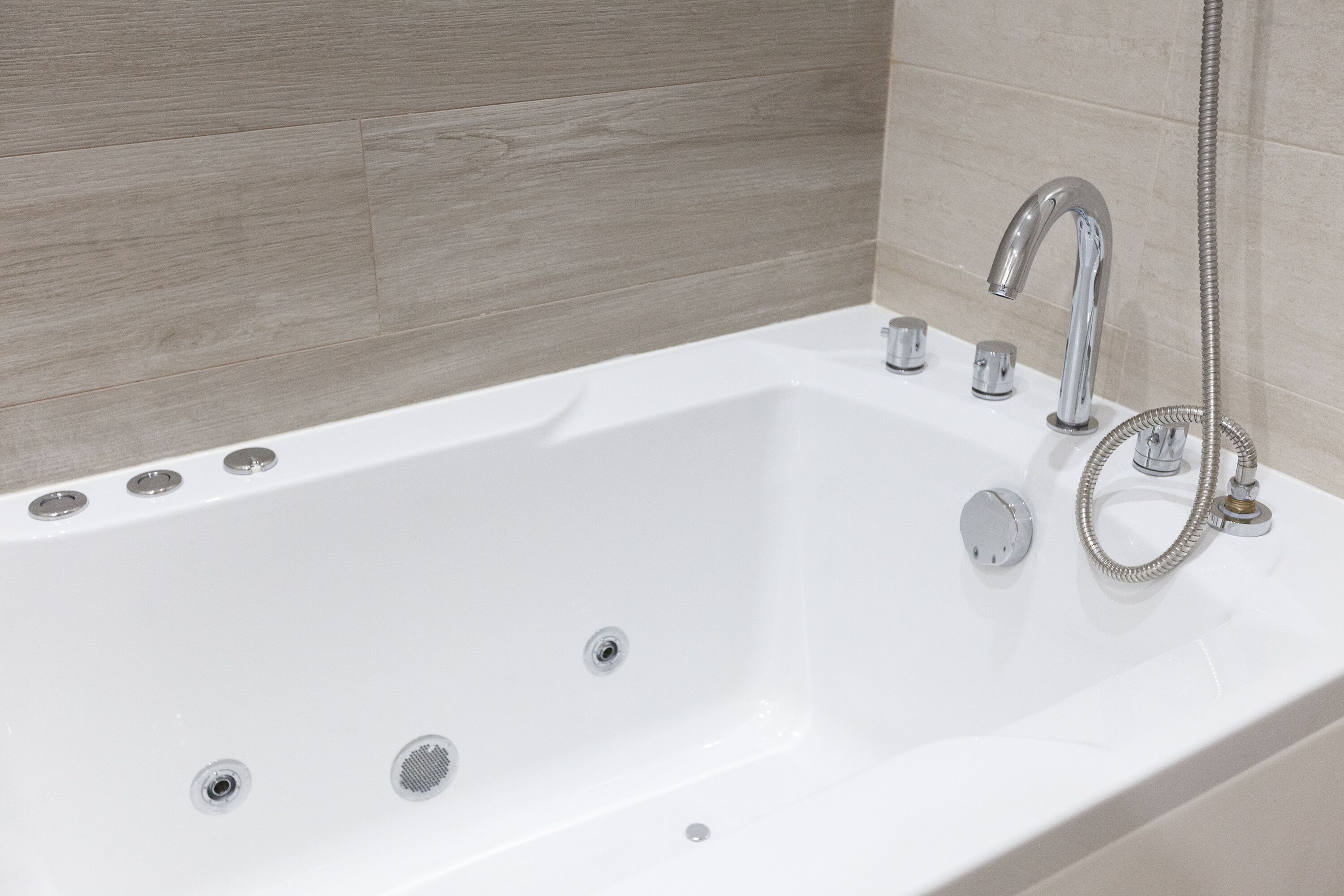 A modern bathroom with a white bathtub, chrome fixtures, and a wooden wall panel.