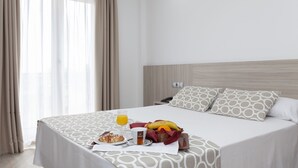 A hotel room with a neatly made bed, a breakfast tray with pastries, a glass of orange juice, and a fruit basket. - Hotel Olympia Ronda II (Puig)