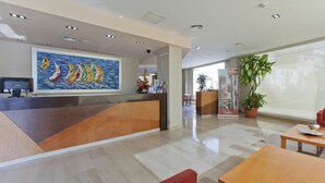 A modern reception area with a wooden reception desk, a large painting of sailboats, and a potted plant. - Hotel Olympia Ronda II (Puig)