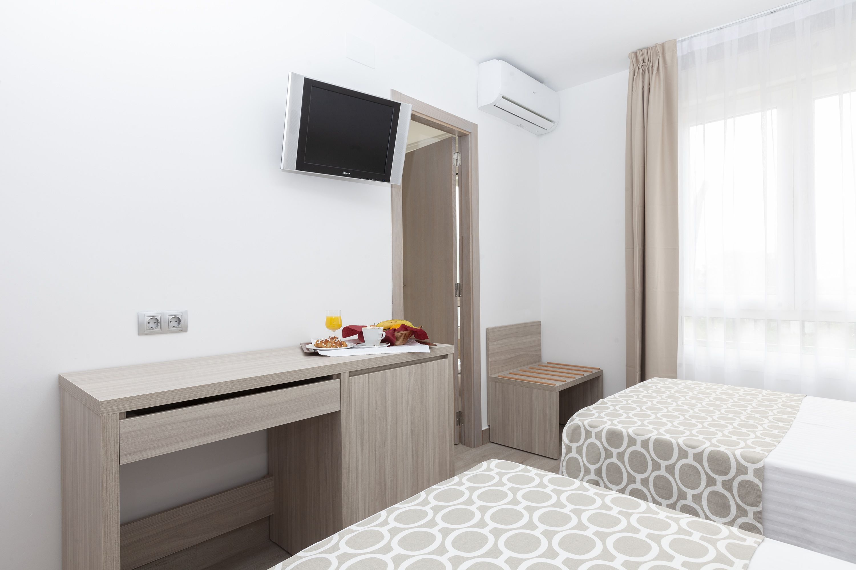 A hotel room with a desk, a bed, a TV, and a window with curtains.