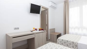 A hotel room with a desk, a bed, a TV, and a window with curtains.