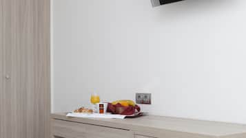 A modern hotel room with a wooden wardrobe, a desk with breakfast items, and a mounted flat-screen TV.
