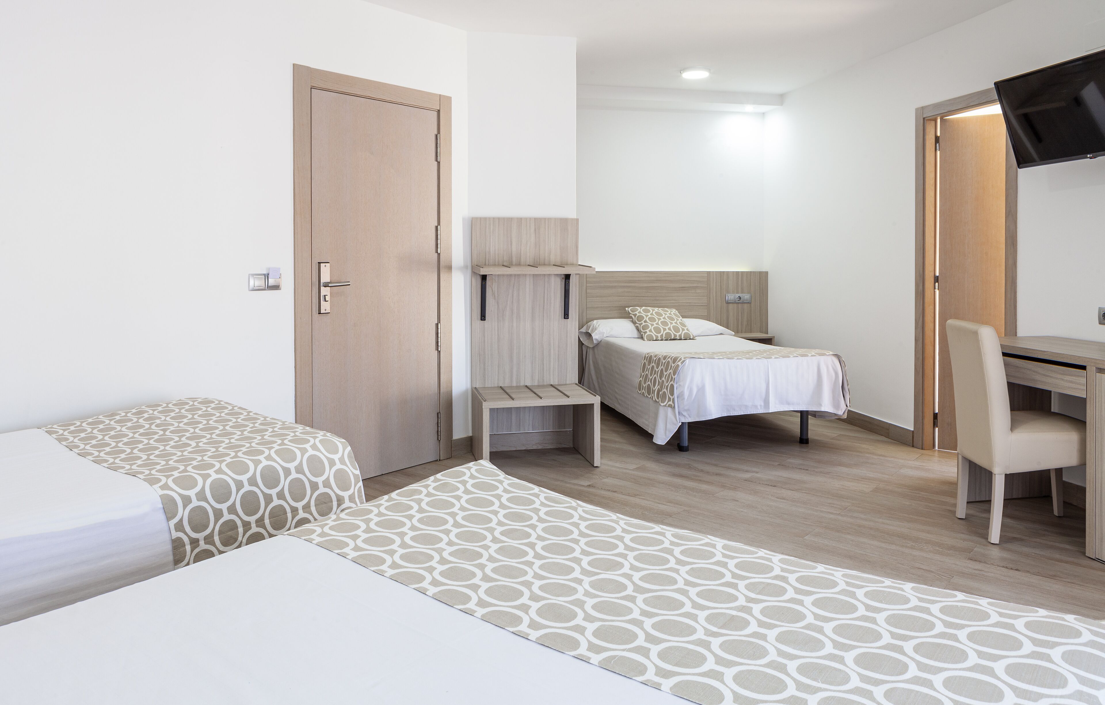 Une chambre d’hôtel avec deux lits, un bureau, une chaise, une télévision et une armoire en bois.