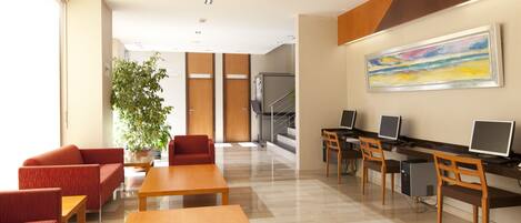 A modern hotel lobby with red seating, a large painting, and a staircase leading to an upper floor.
