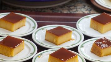 Una mesa con varios platos de flan de caramelo y un bol de fruta cortada al fondo.