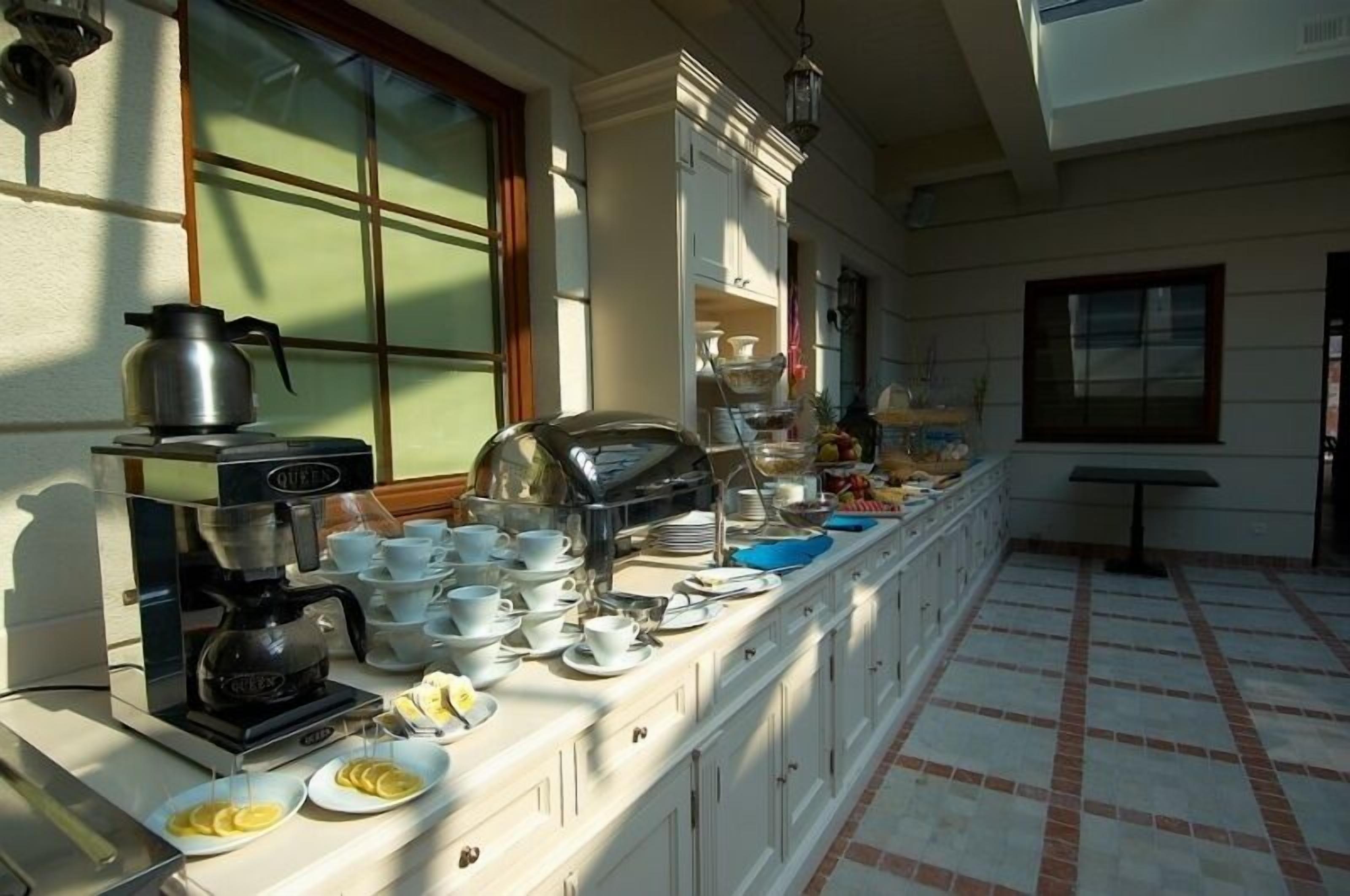 A breakfast buffet setup with a coffee maker, cups, plates, and a fruit bowl.