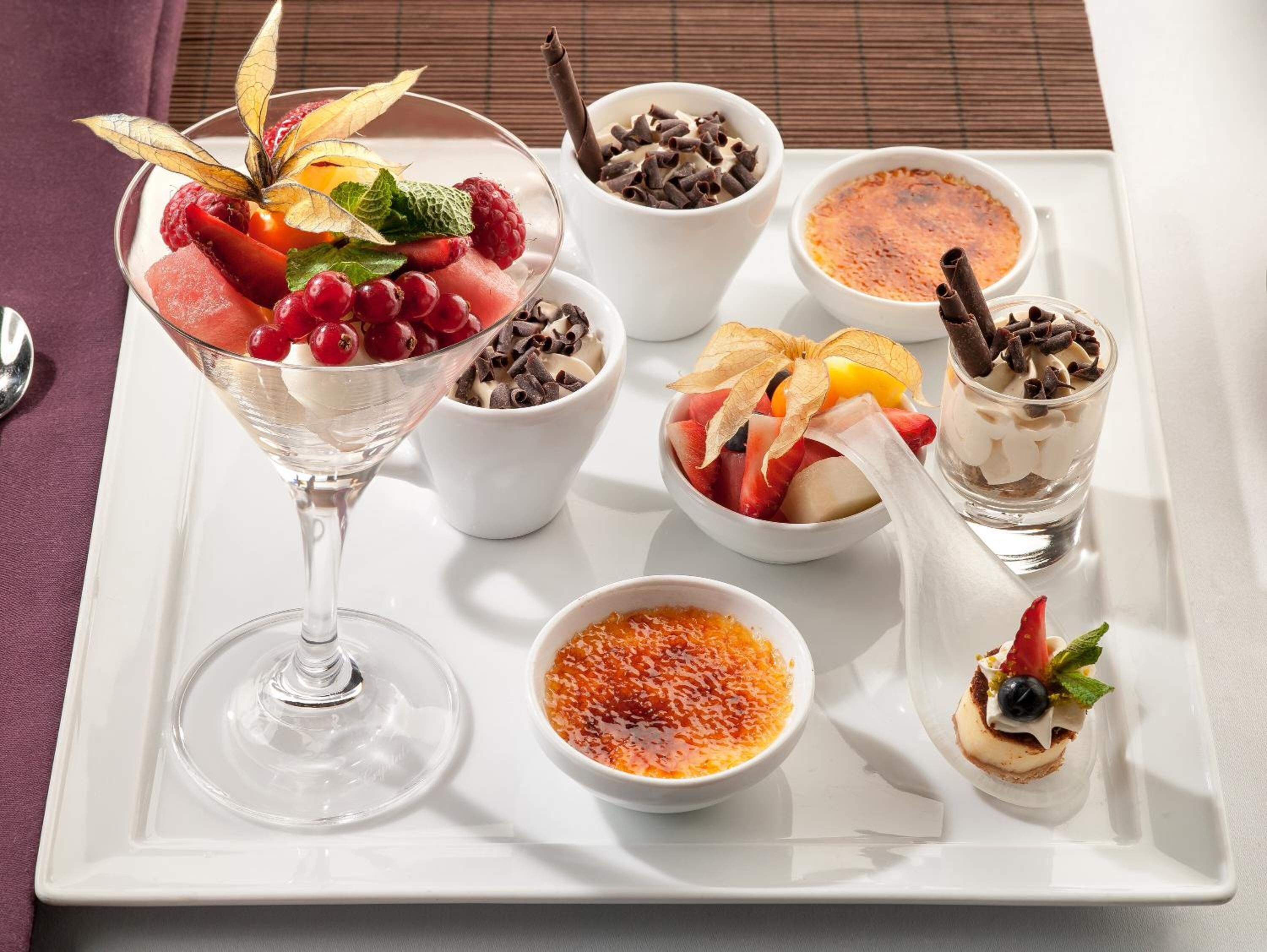 A variety of desserts on a white tray, including a glass of a creamy dessert, bowls of chocolate and fruit, and a small dish of red caviar.
